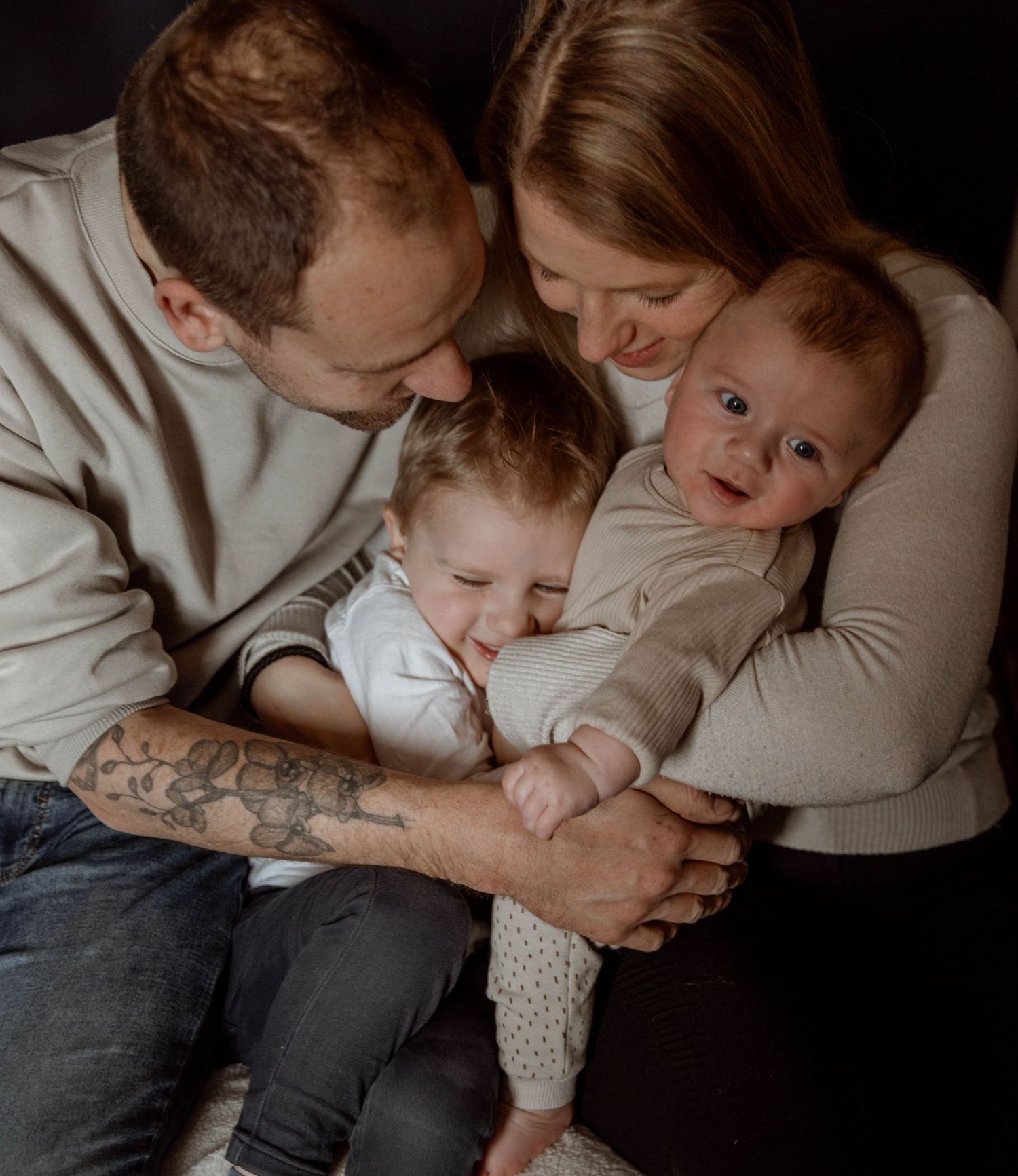 Cozy family moment with parents cuddling children on dark background.