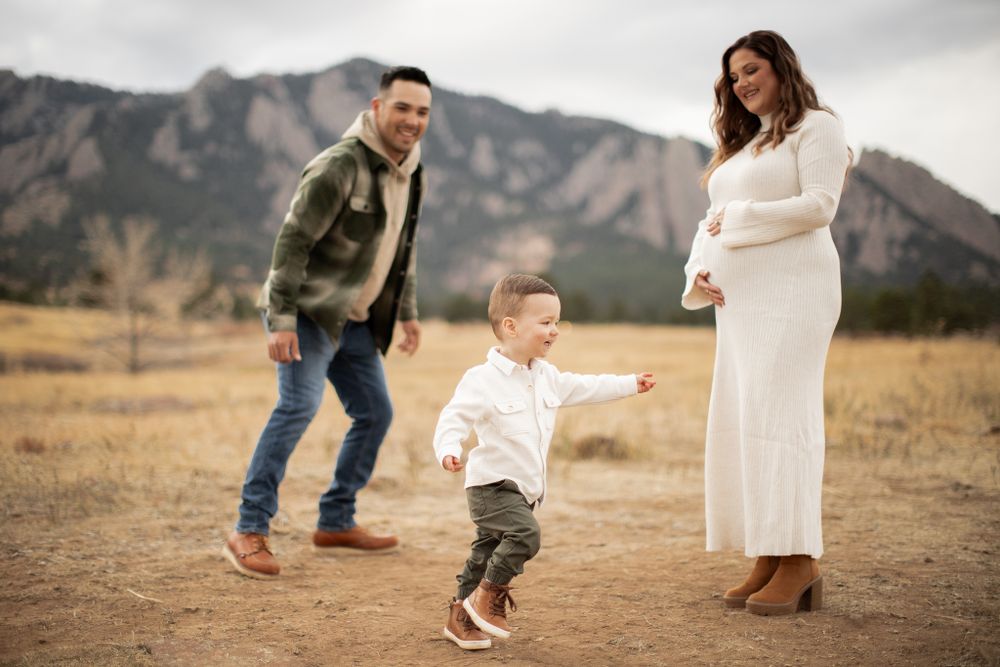Family in casual attire plays together in an outdoor field with dramatic mountain backdrop in Boulder, Colorado.