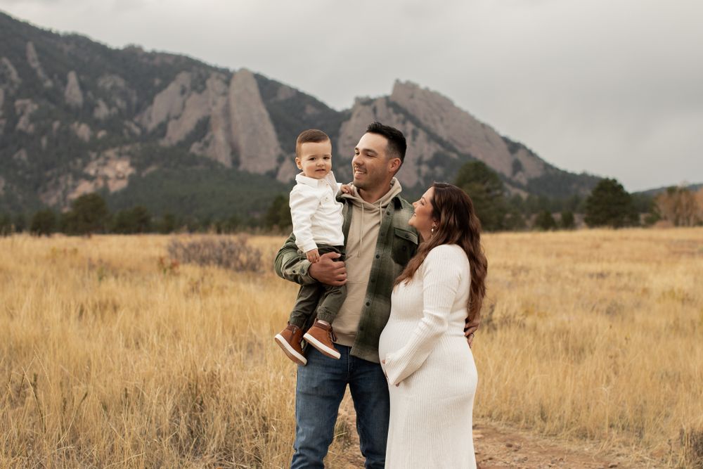 A family stands together in a golden grassy field with majestic Flatiron mountains visible in Boulder, Colorado.