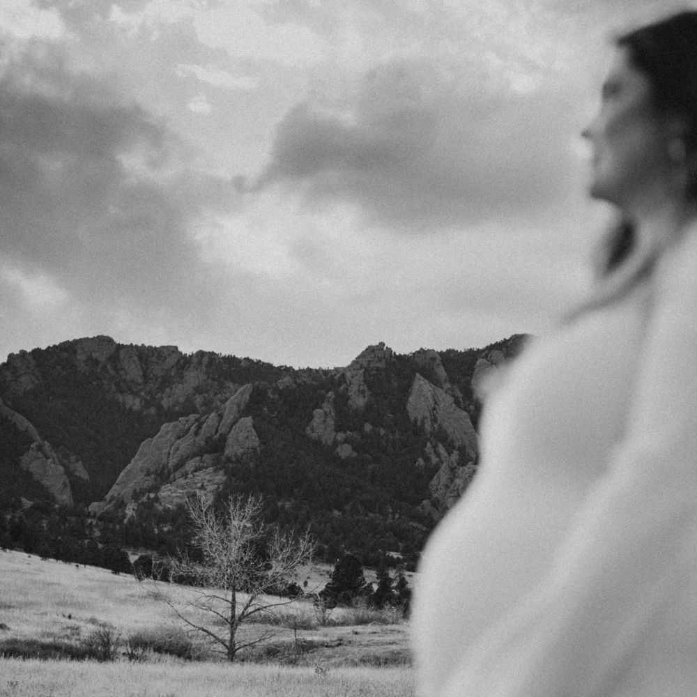 A dramatic black and white landscape photograph showing a silhouetted figure against rocky mountain backdrop and cloudy sky.