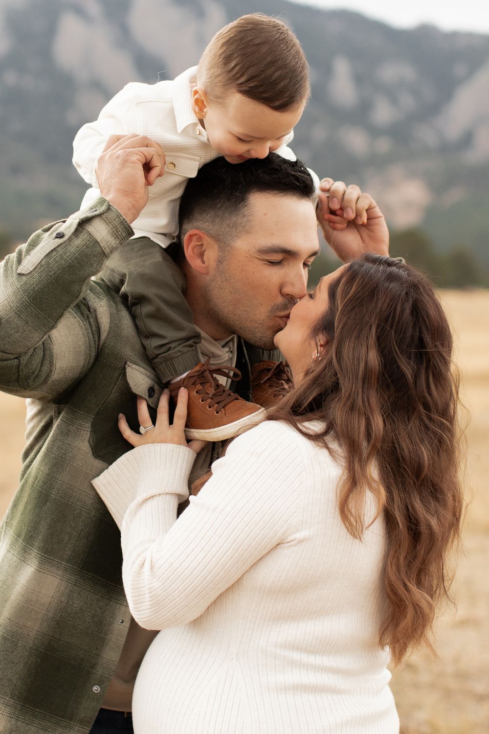 A loving family shares an intimate moment together against a mountain backdrop in a grassy field.