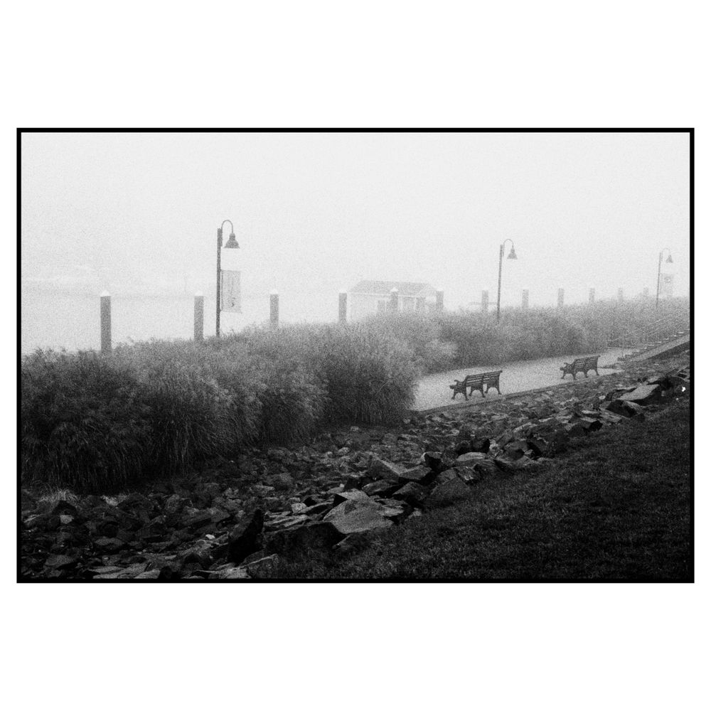 A foggy industrial landscape with utility poles and buildings visible in the misty distance along a rocky path.