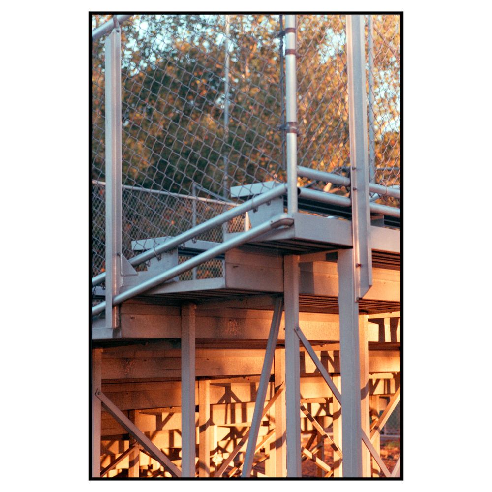 Metal staircase and railing against autumn trees with stacked firewood storage underneath the wooden deck structure.