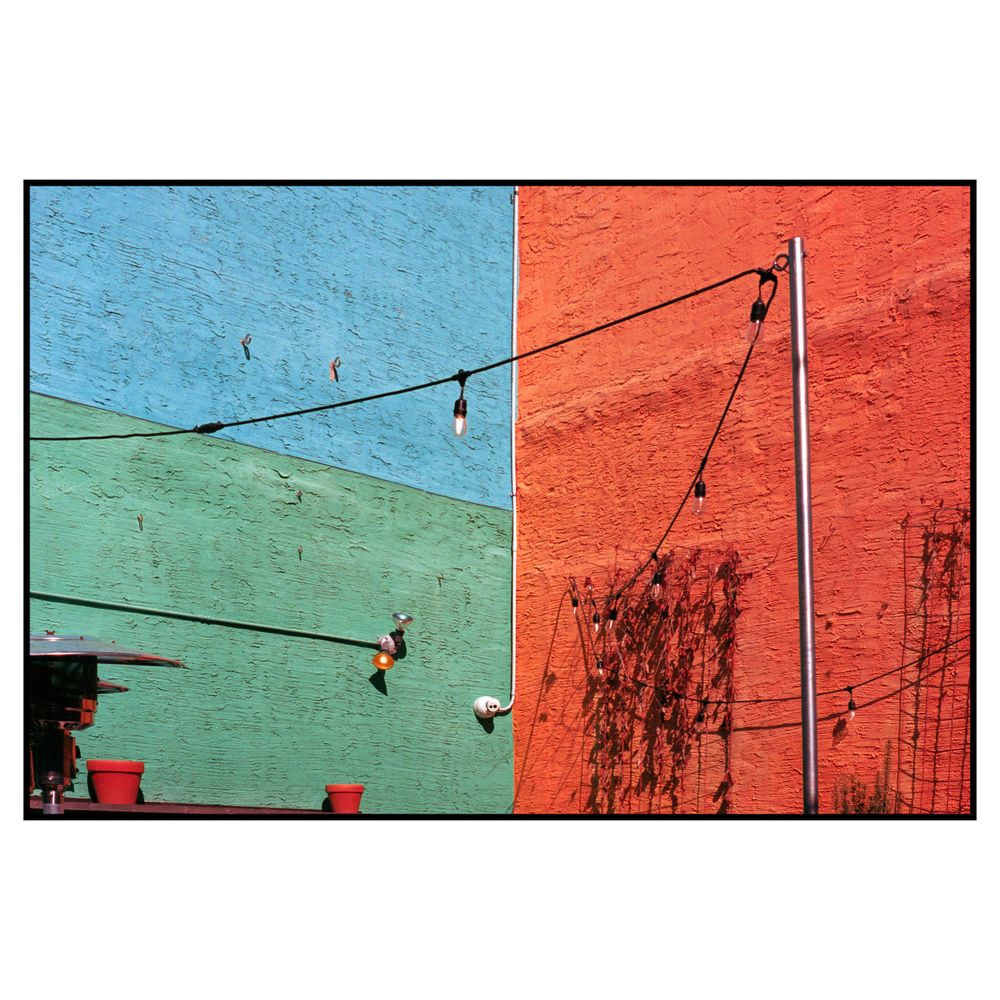 Colorful architectural photograph featuring green and orange walls with hanging string lights against a bright blue sky.