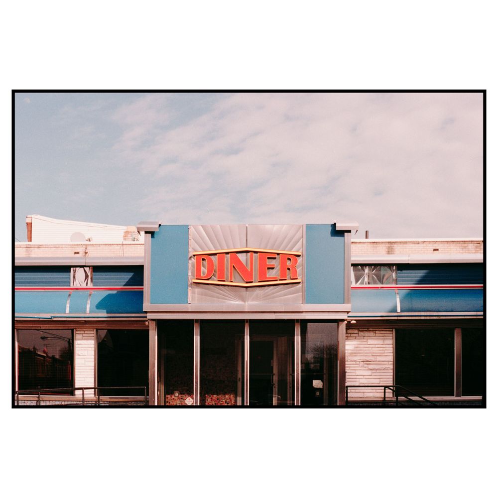Vintage American diner exterior with retro neon sign and blue trim under pastel sunset sky.
