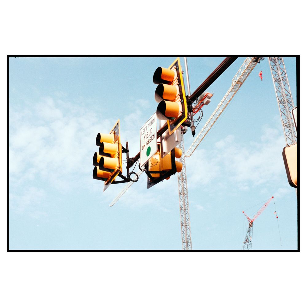 Yellow traffic signals mounted on metal poles against a blue sky with construction cranes visible in the background.
