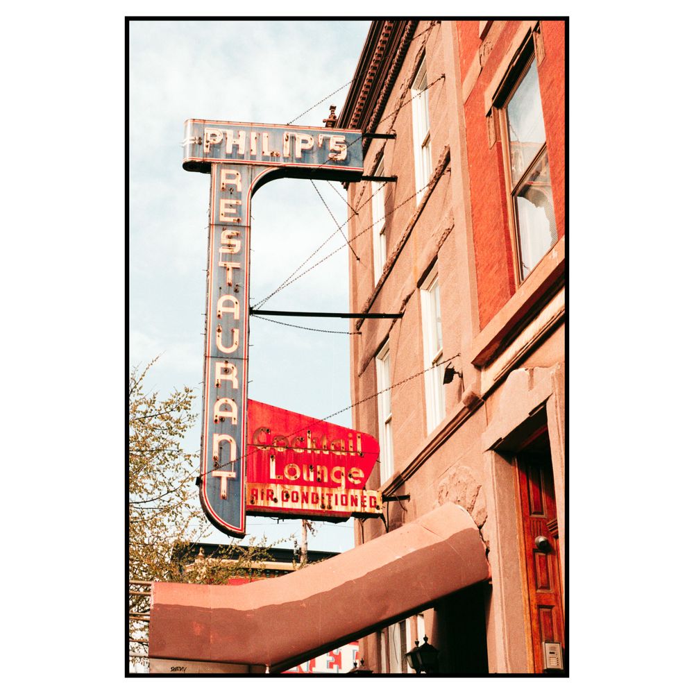 A vintage Phillips restaurant sign with neon lettering mounted on a brick building facade in warm tones.