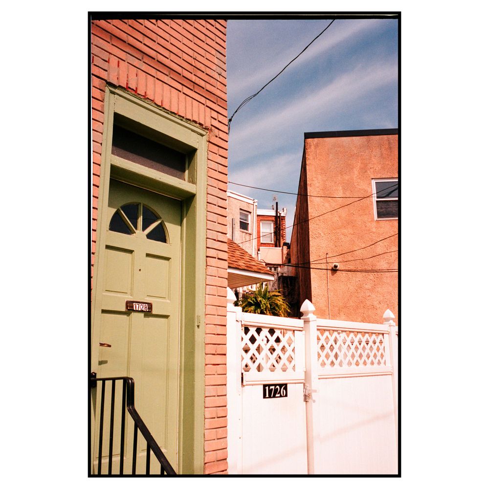 A light green door with arched glass panels on a salmon-colored brick building next to a white lattice fence.