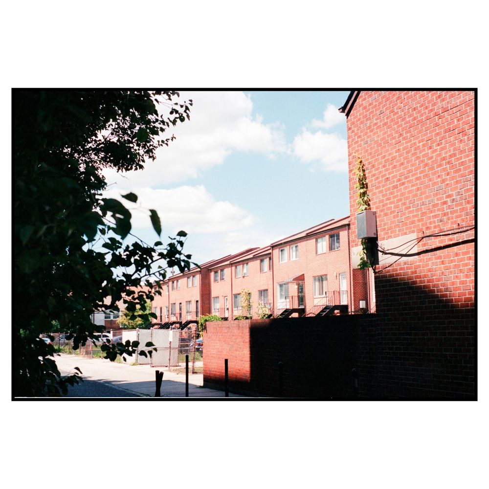 Pink townhouses and brick buildings line a residential street on a sunny day with blue skies and trees.