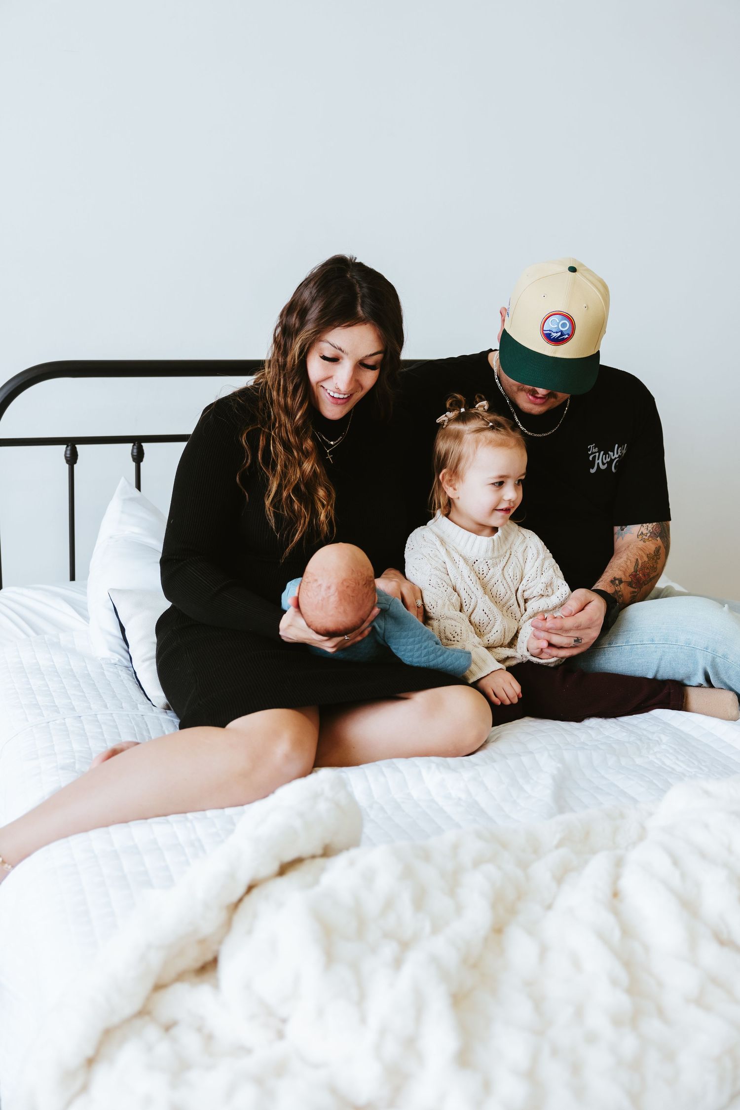 Family relaxing together on a bed with white linens.
