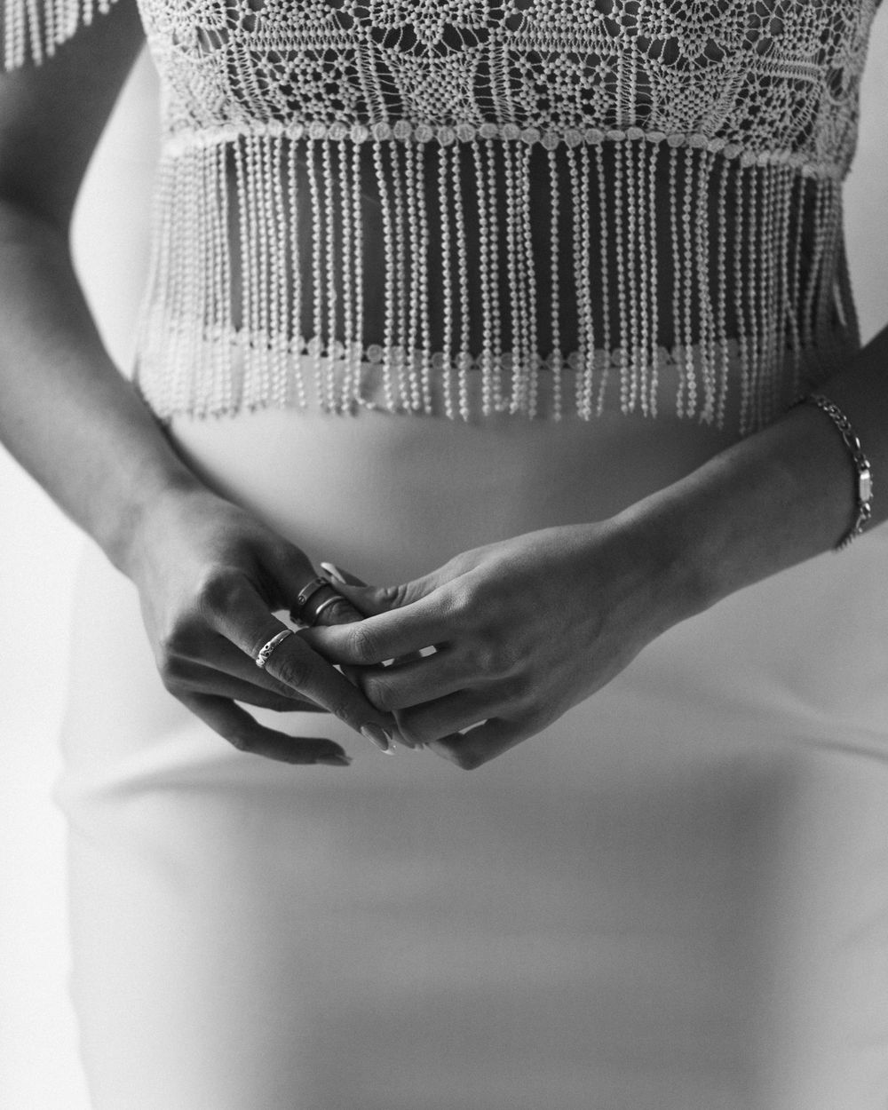Close-up of hands and detailed beadwork on elegant white wedding dress.