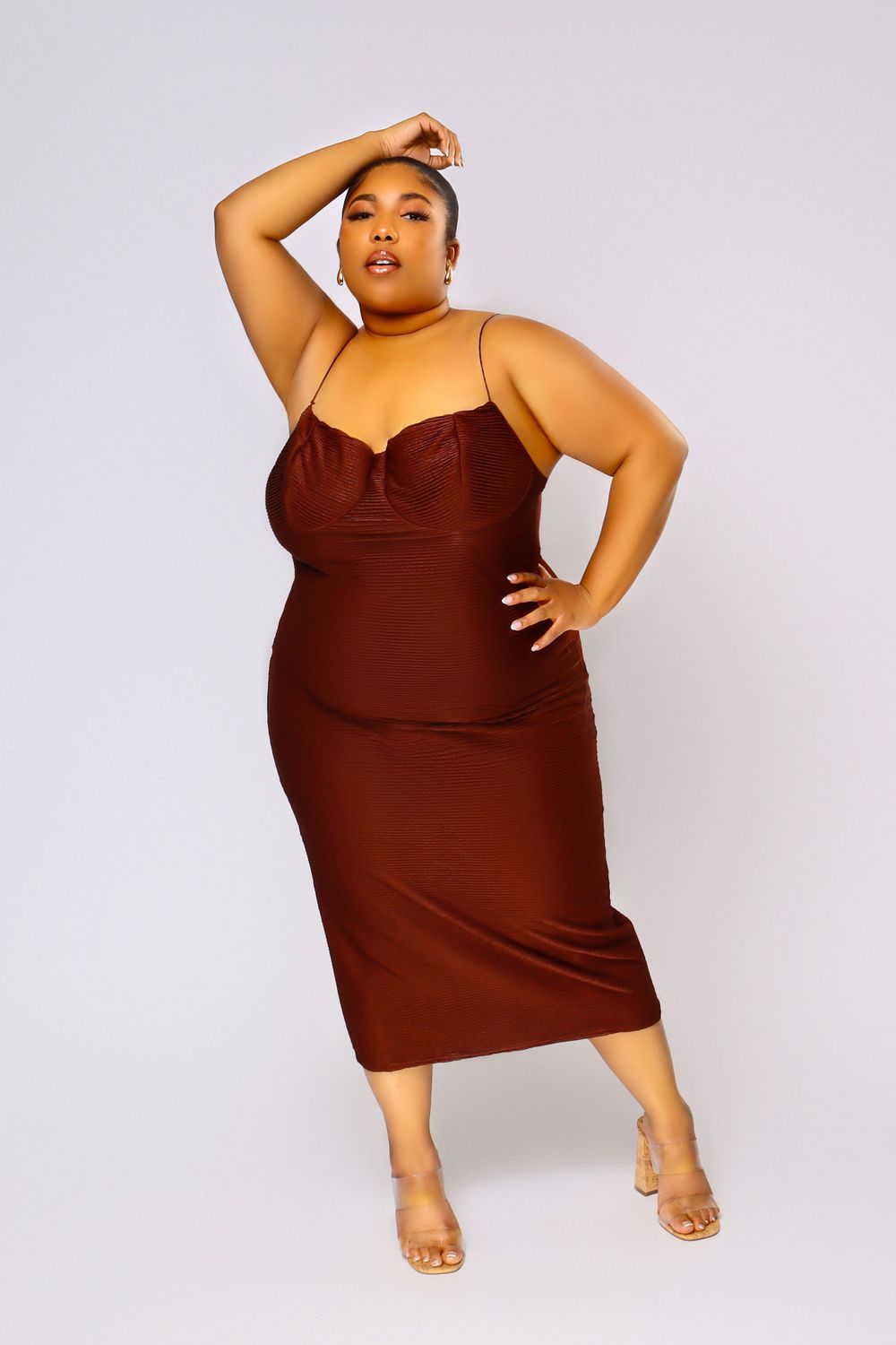 Curvy model in burgundy bodycon dress poses confidently against light background.
