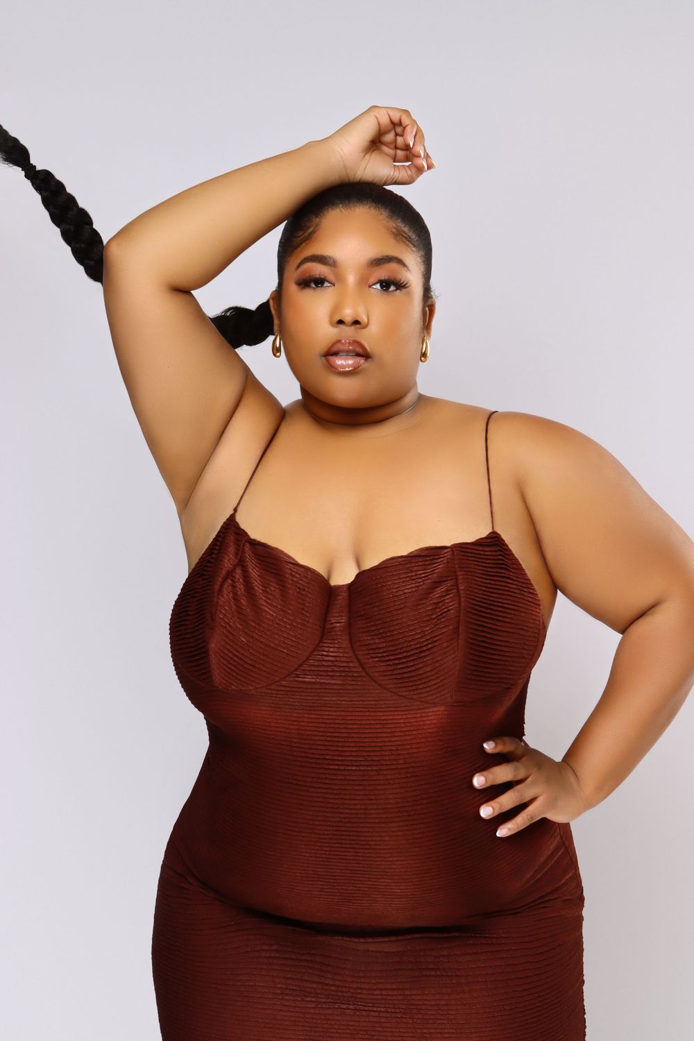 Plus size model in burgundy dress poses elegantly against light background.