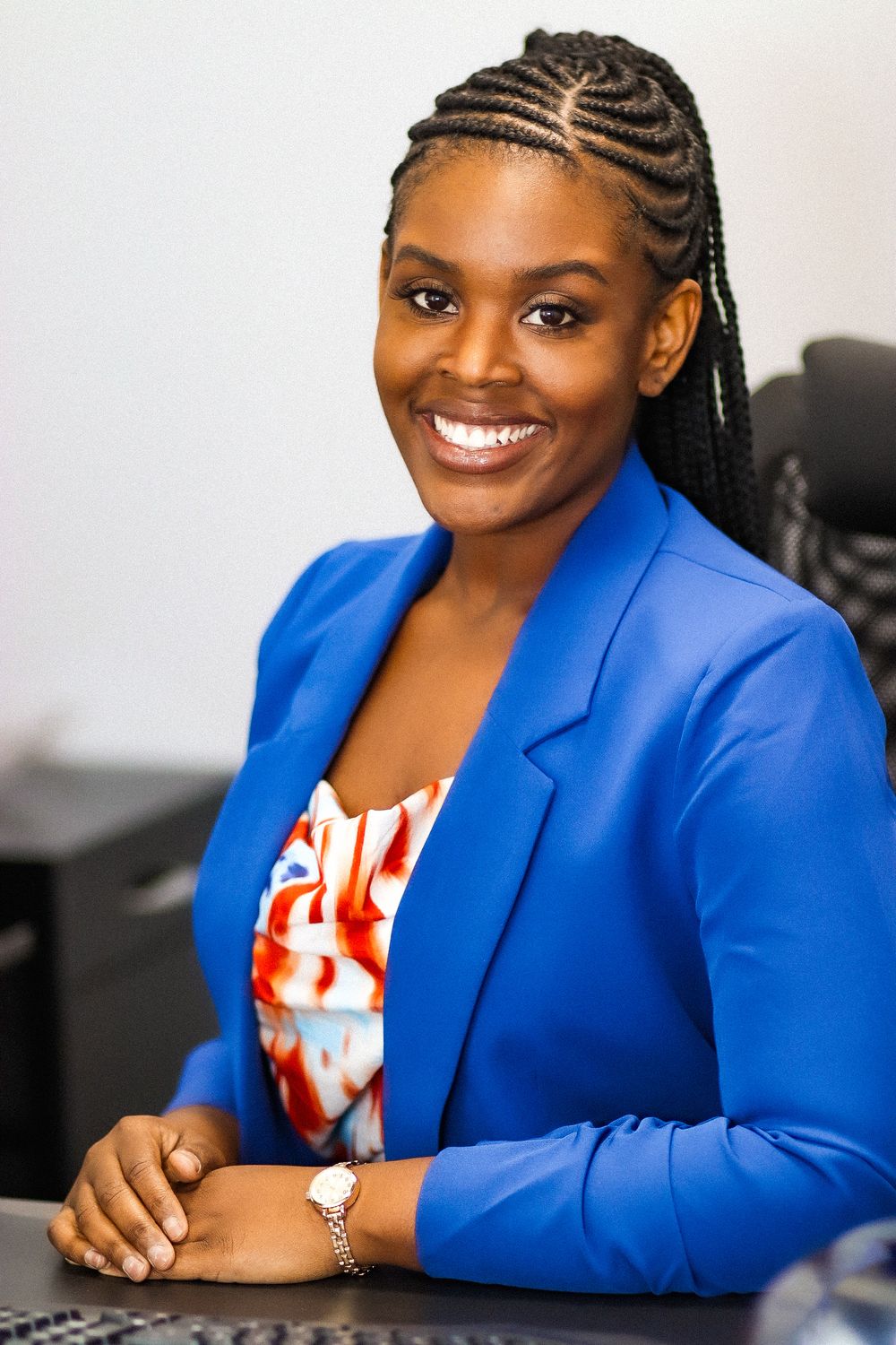Professional in royal blue blazer and patterned top seated at desk with welcoming smile.