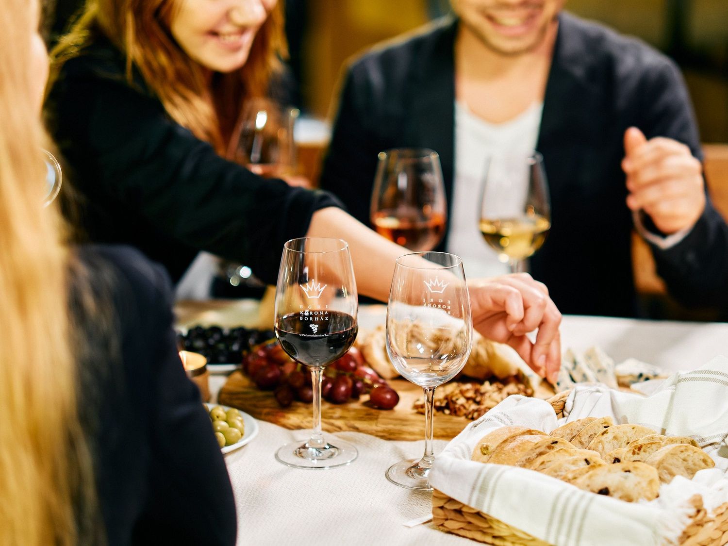 People enjoying wine and appetizers at a restaurant table with glasses of red and white wine.