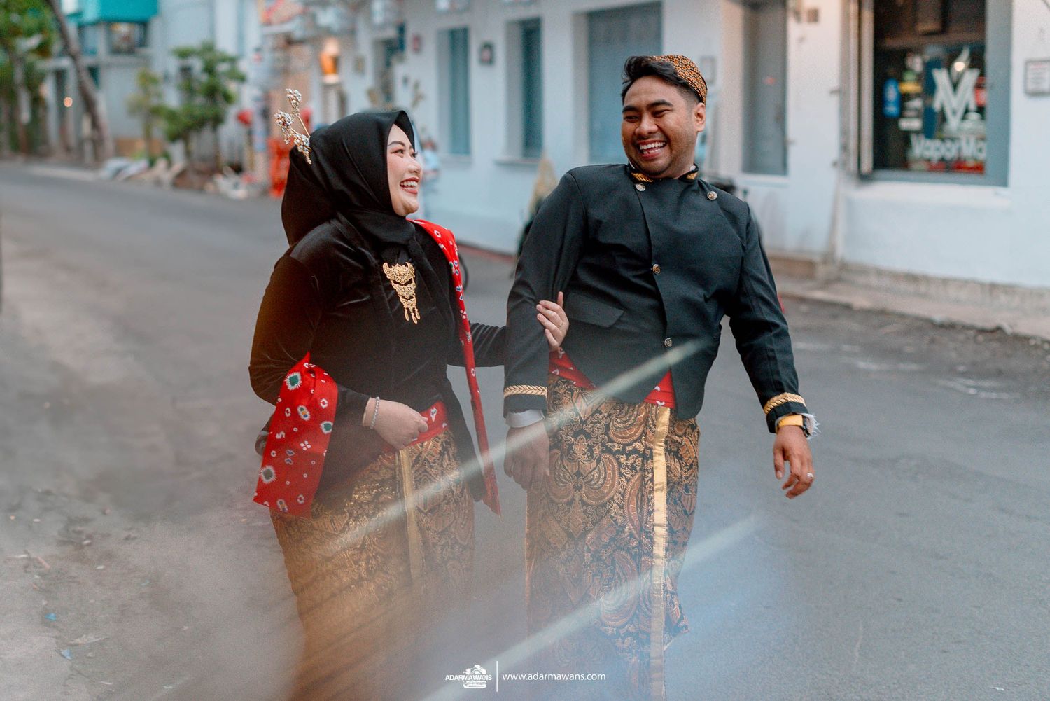 A couple shares a romantic moment walking on a city street, her red dress flowing in the breeze.