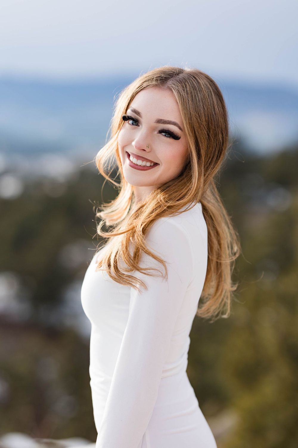 Beautiful portrait of someone in a fitted white long-sleeve dress posing against a soft blurred outdoor background.