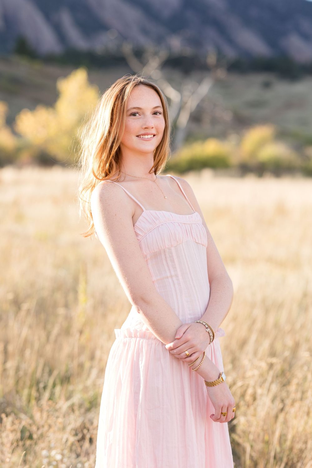 A person in a flowing white dress stands in a golden sunlit field during golden hour.