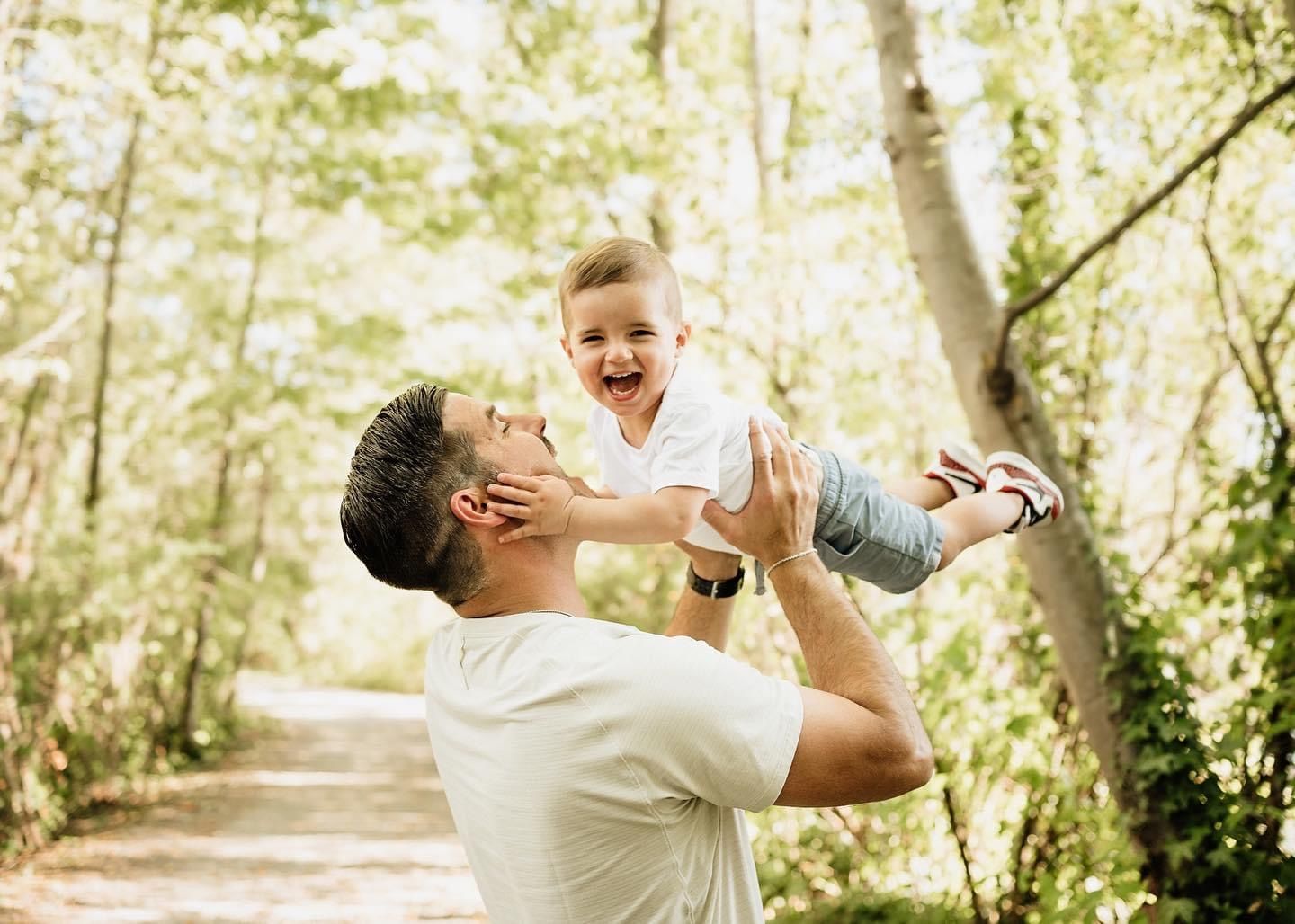 A joyful moment captured on a sunlit forest path as a child is lifted high in the air during playtime.