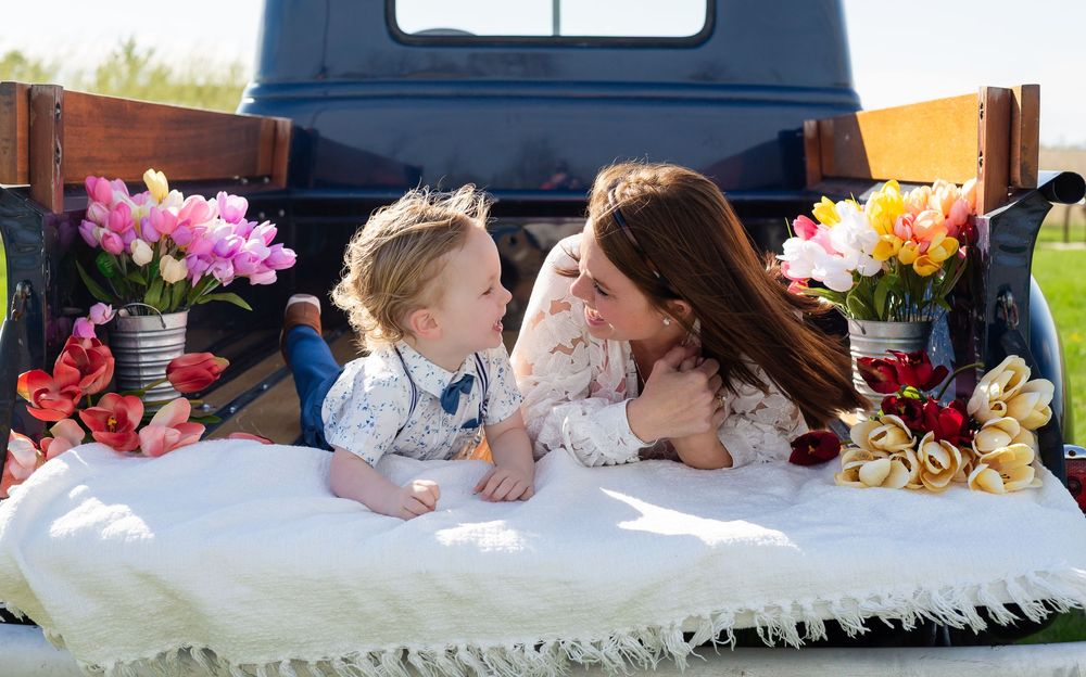 A sweet moment captured in the back of a truck bed with cushions and colorful flower bouquets surrounding the scene.