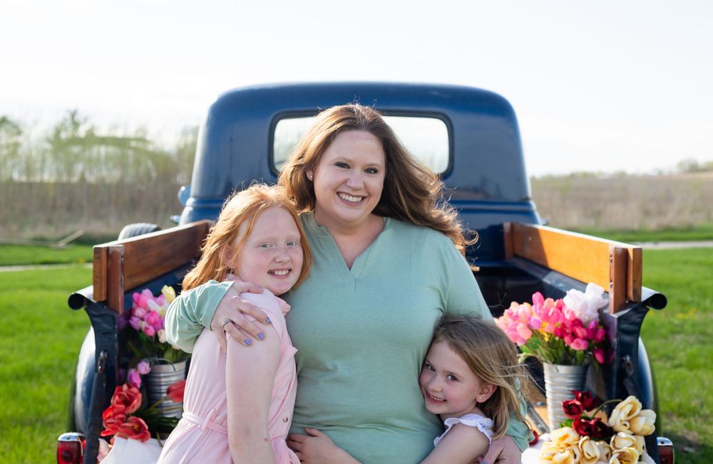 A family poses together in the bed of a vintage blue truck filled with colorful spring flowers.
