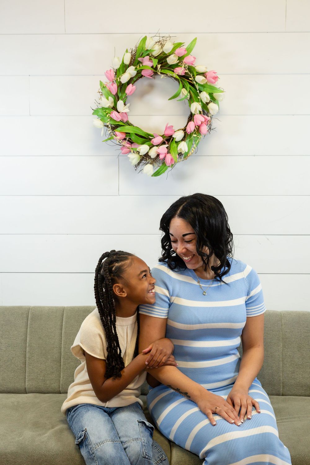 A spring tulip wreath with pink and white flowers hangs above a cozy gray couch where people share a joyful moment together.
