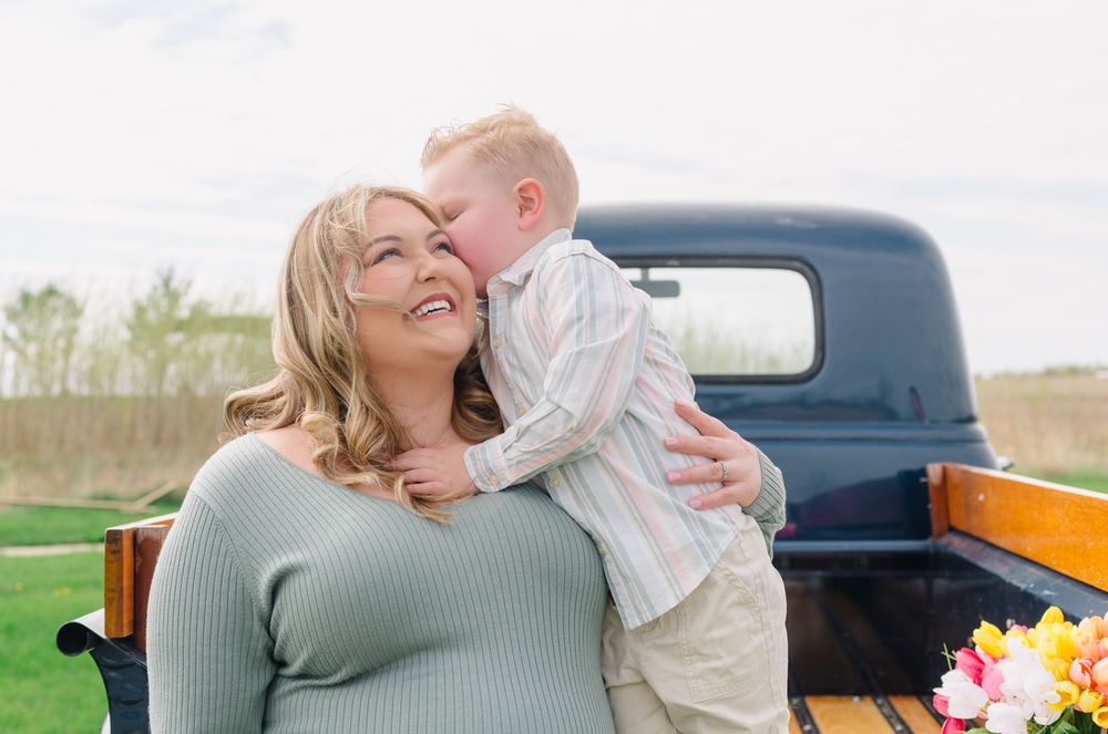 A heartwarming candid outdoor moment shared between two people next to a vintage blue truck with flowers visible.