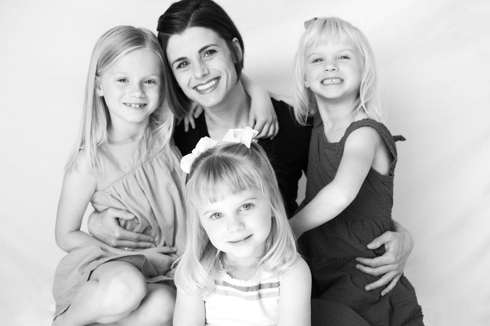 Black and white studio portrait of a family group with three children smiling together against a white background.