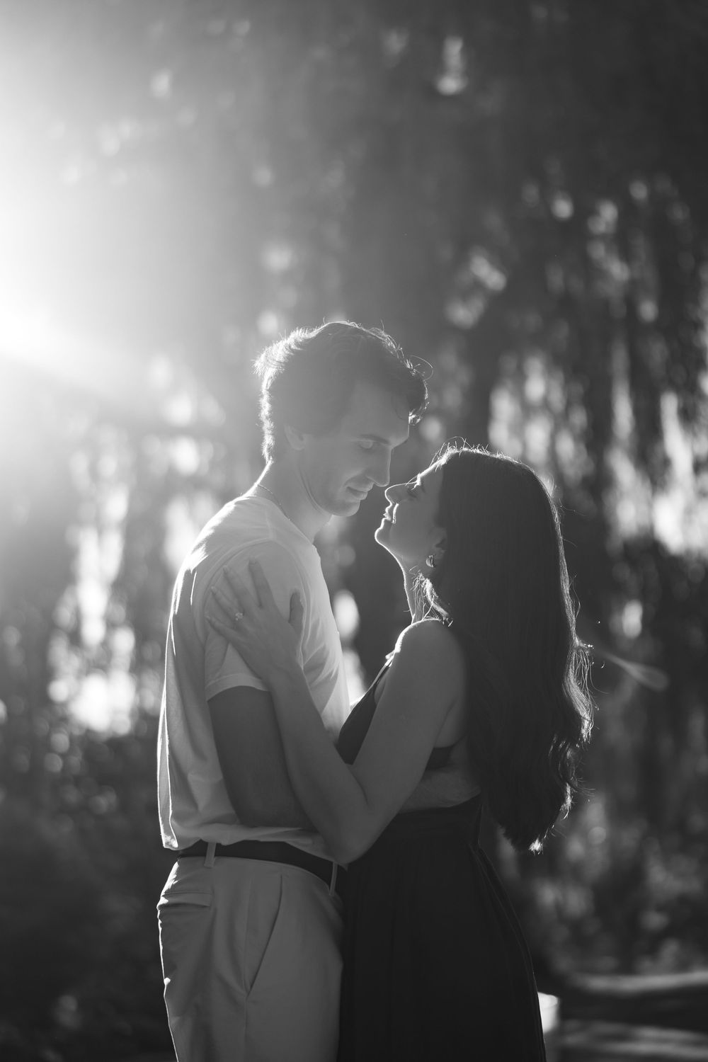 A silhouetted couple shares an intimate moment in dreamy backlit forest setting during golden hour.
