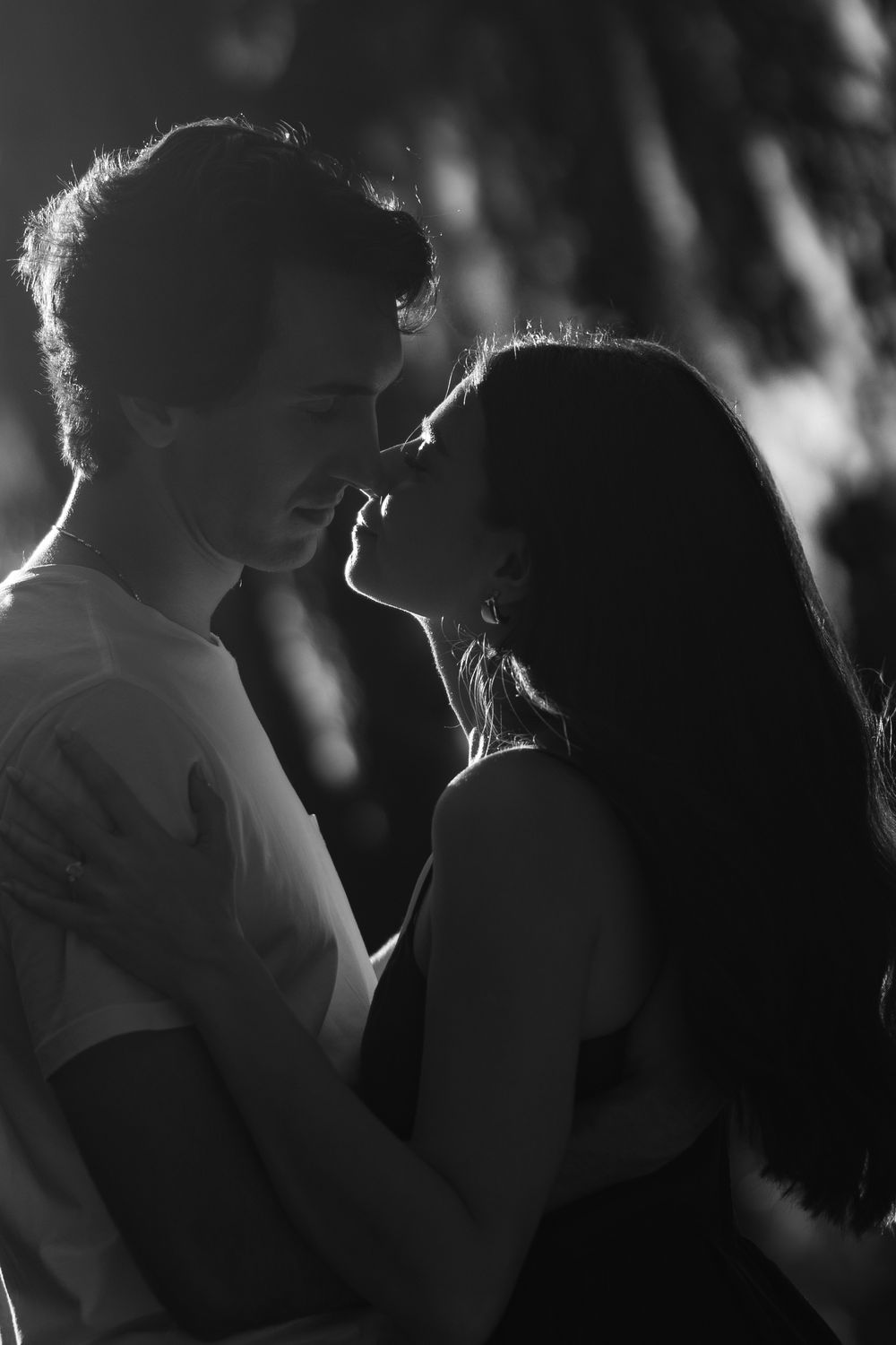 A romantic black and white silhouette of a couple embracing in soft backlight with glowing rim lighting around their forms.