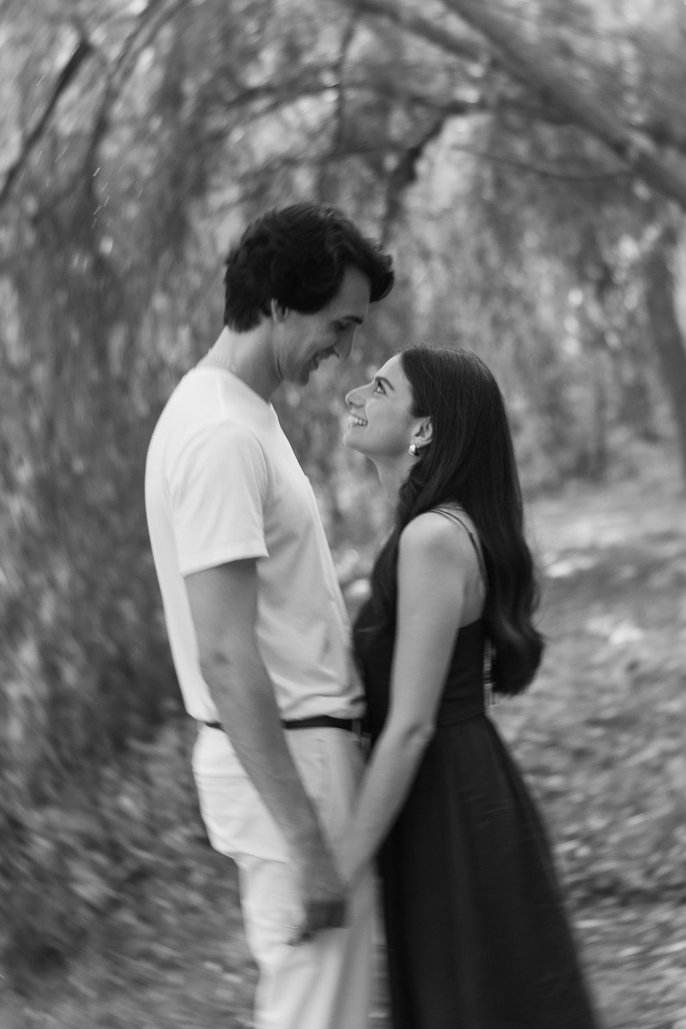 A romantic couple shares an intimate moment in a dreamy black and white forest setting.