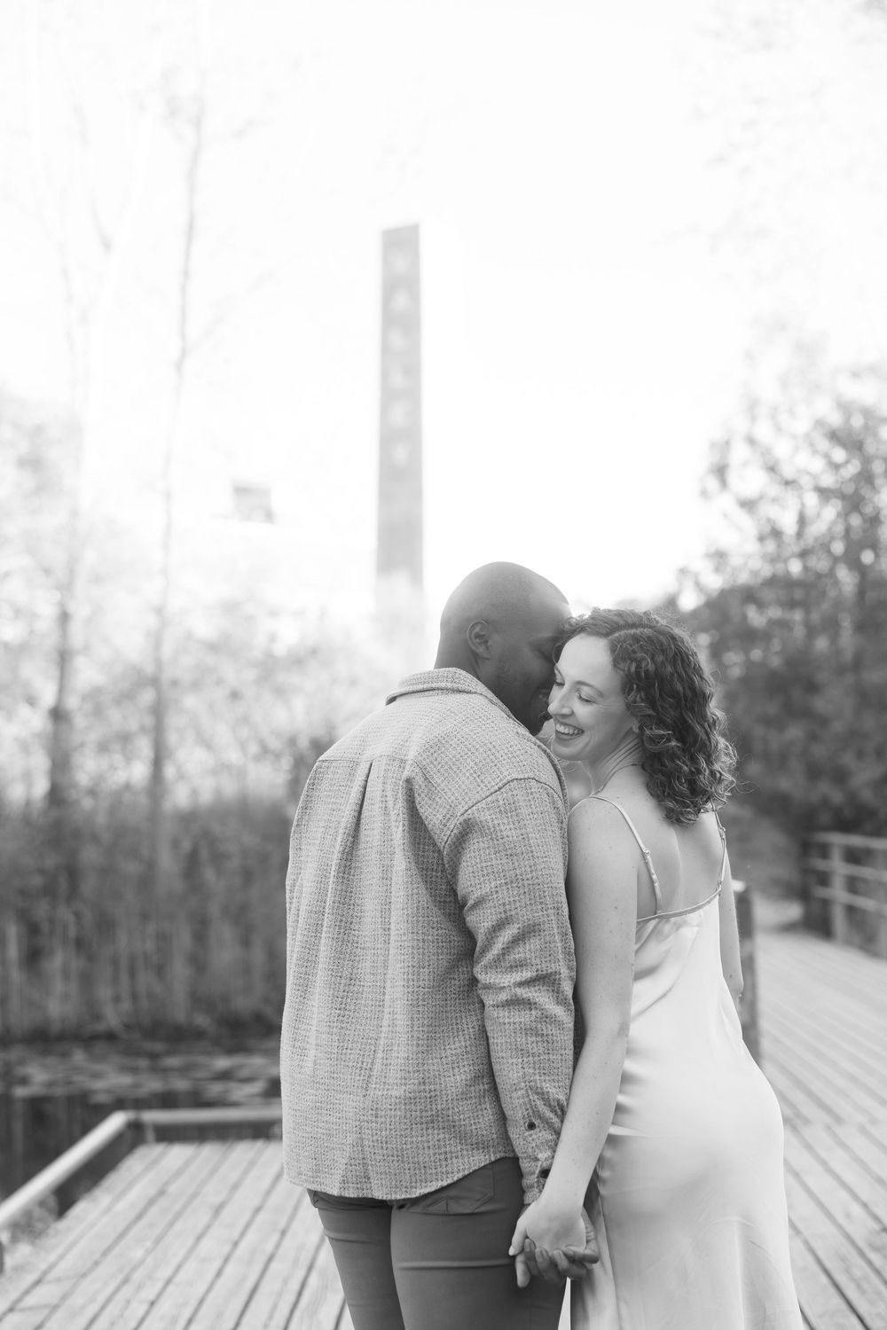 A romantic couple shares tender moments in black and white photos on a wooden deck surrounded by trees.