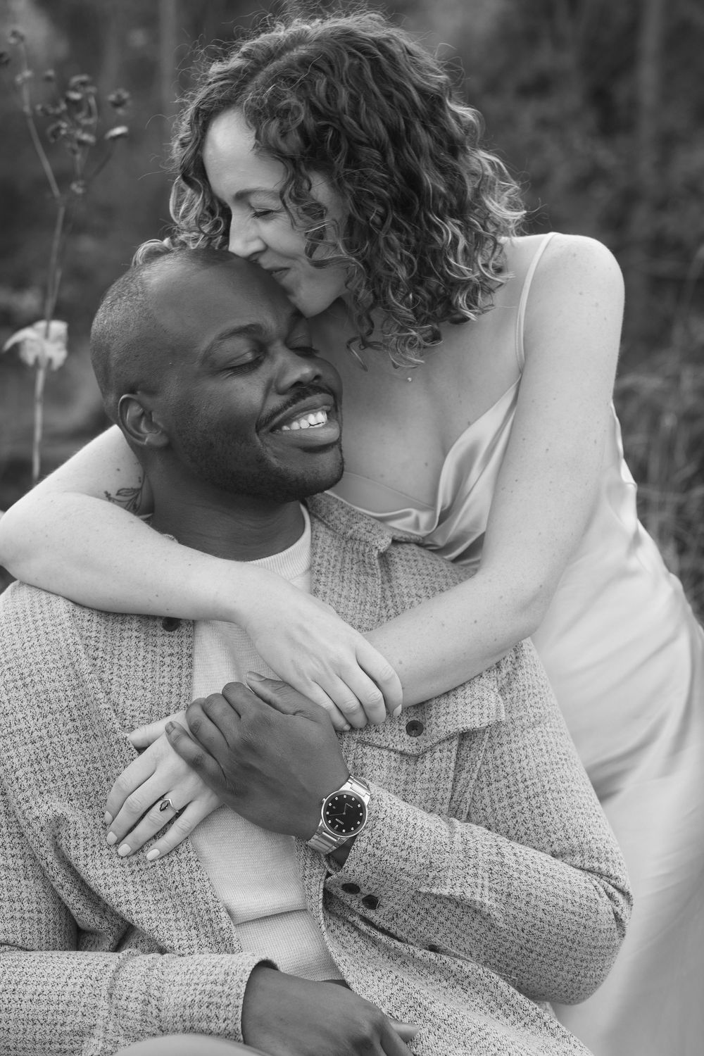 A loving couple embraces in a tender black and white portrait, sharing a joyful intimate moment outdoors.