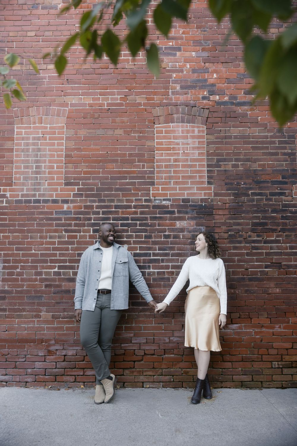 Three connected images show two people sitting against a brick wall with tree leaves visible above.
