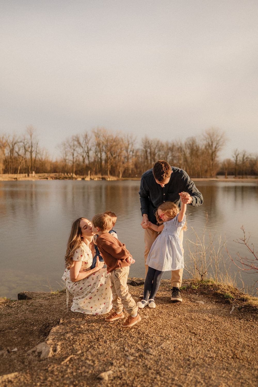 Family gathering by a serene lake at sunset with golden light reflecting off the water.
