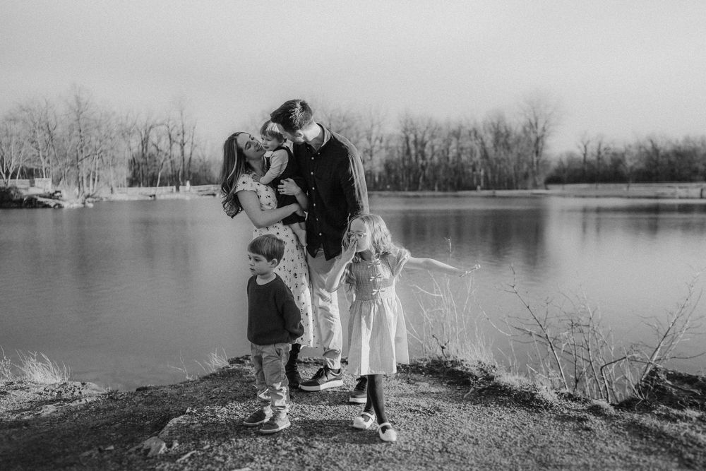 A black and white photograph of a tender family moment by a serene lake on a winter day.