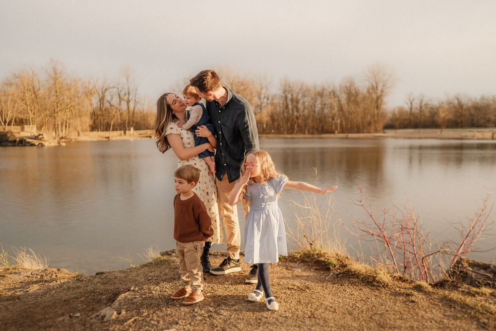 A family shares a tender moment together while standing on the shoreline of a serene lake at golden hour.