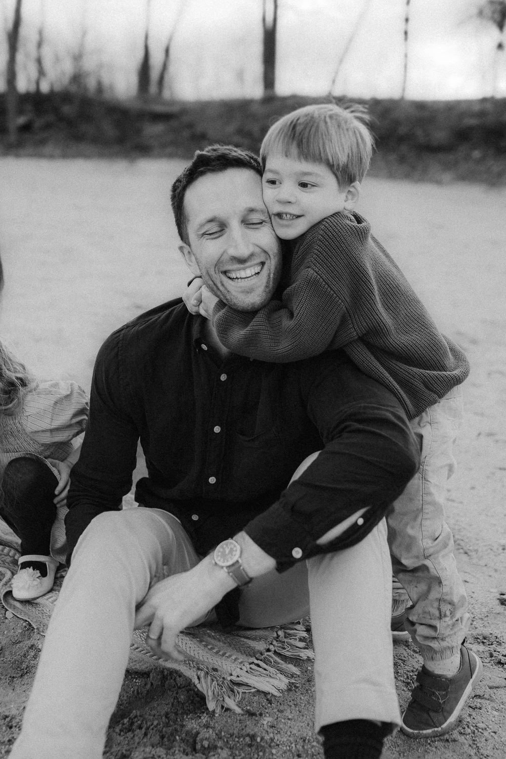 A black and white portrait of a playful parent and child hugging and smiling outdoors.