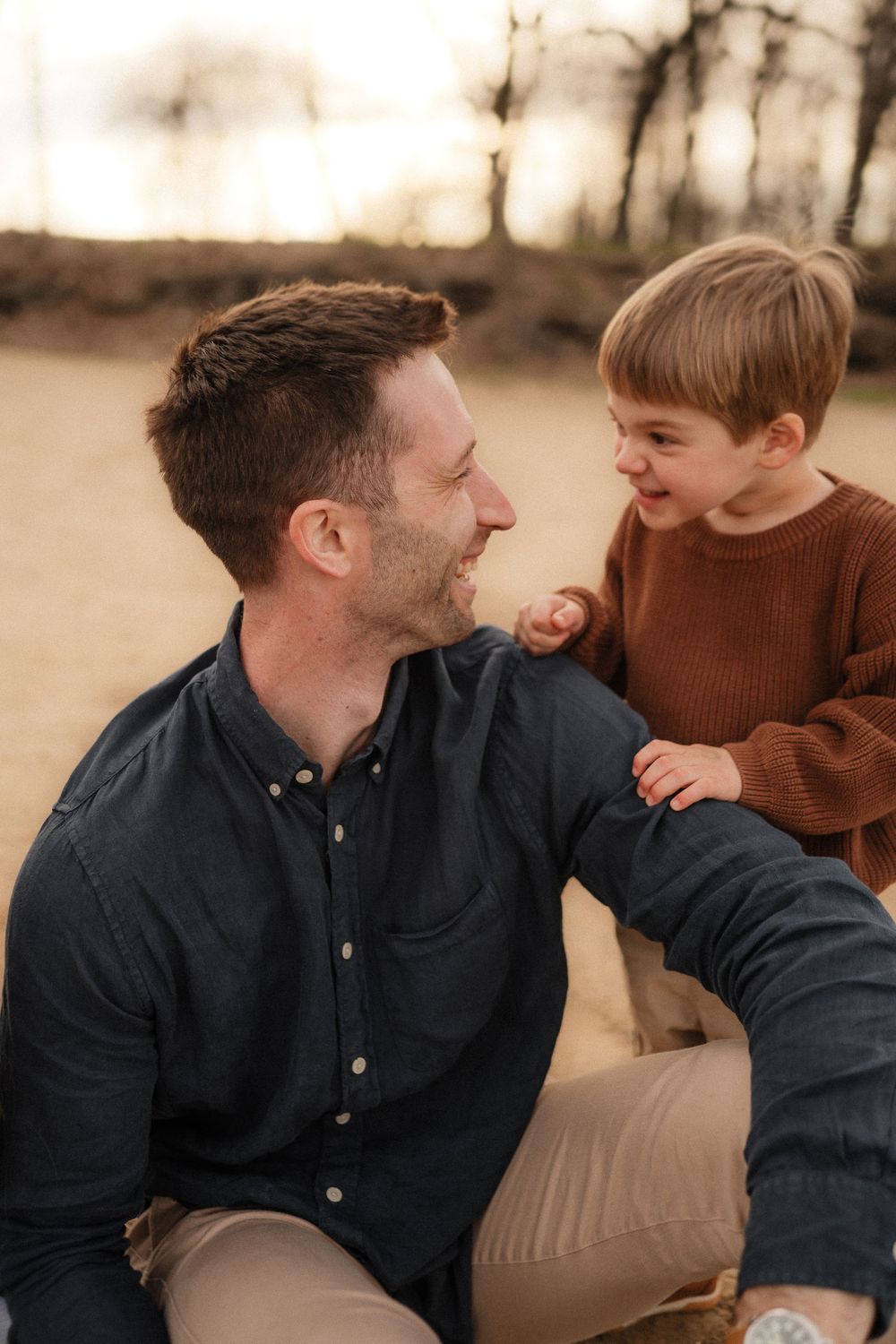 A parent and young child share a joyful moment together outdoors during golden hour.