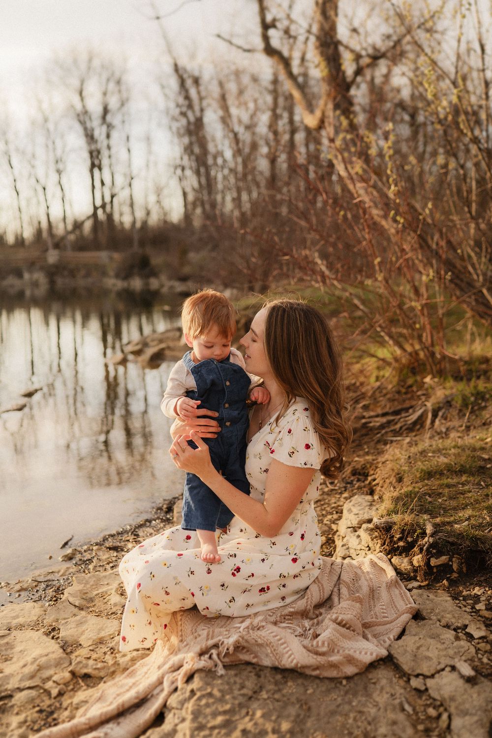 A tender moment captured at sunset by a tranquil lake with fall foliage in the background.