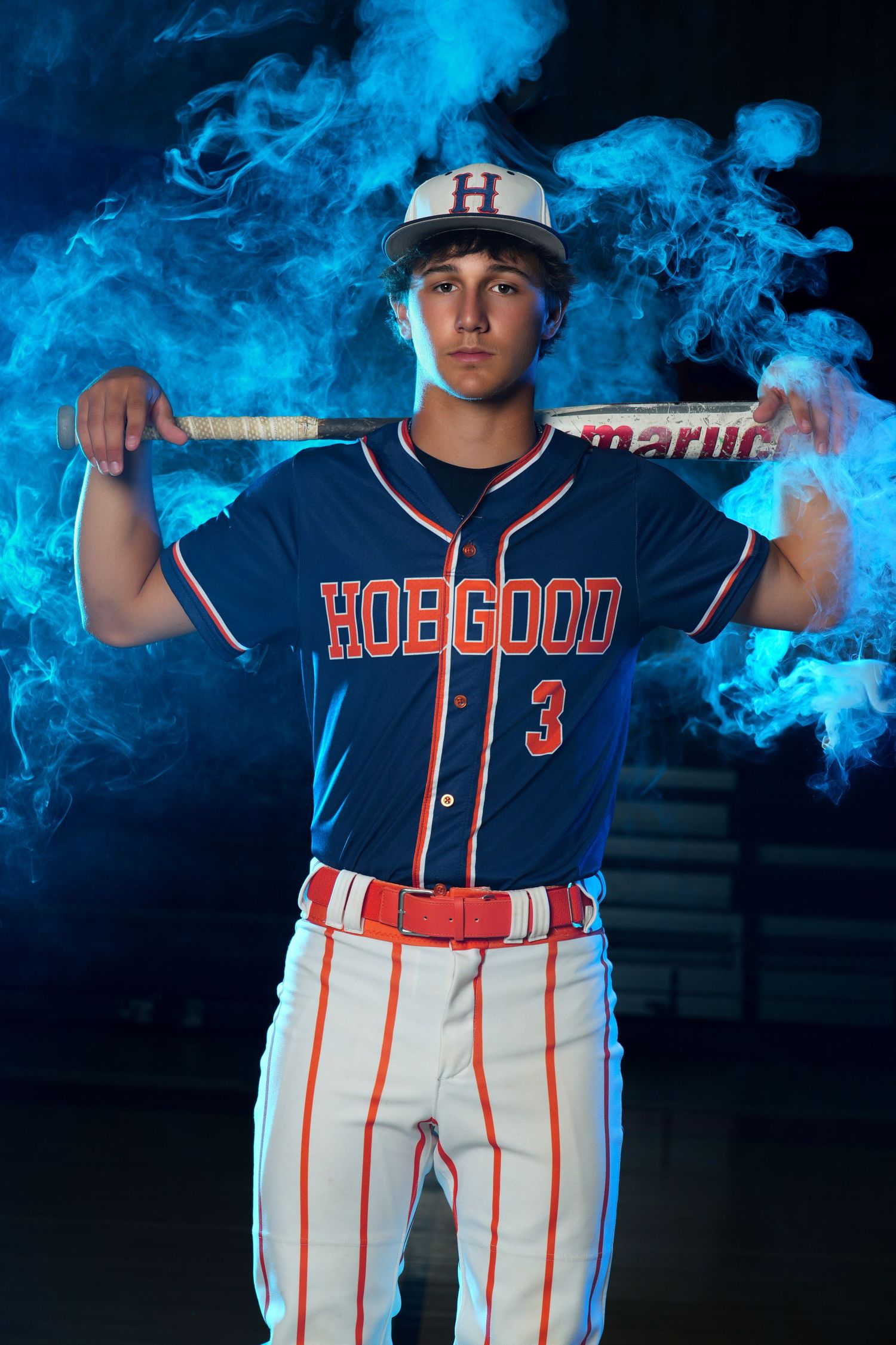 Baseball player in navy Hoegood jersey number 3 poses with bat against dramatic blue smoke background.