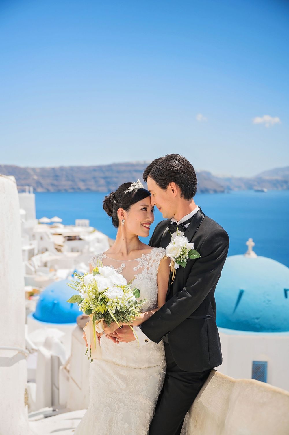 Romantic wedding portrait with Santorini's signature white architecture and blue domes in the background.