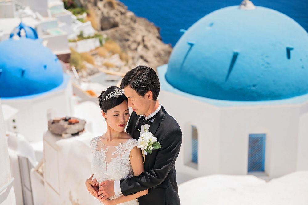 Wedding couple embracing in front of blue-domed churches in Santorini's picturesque landscape.