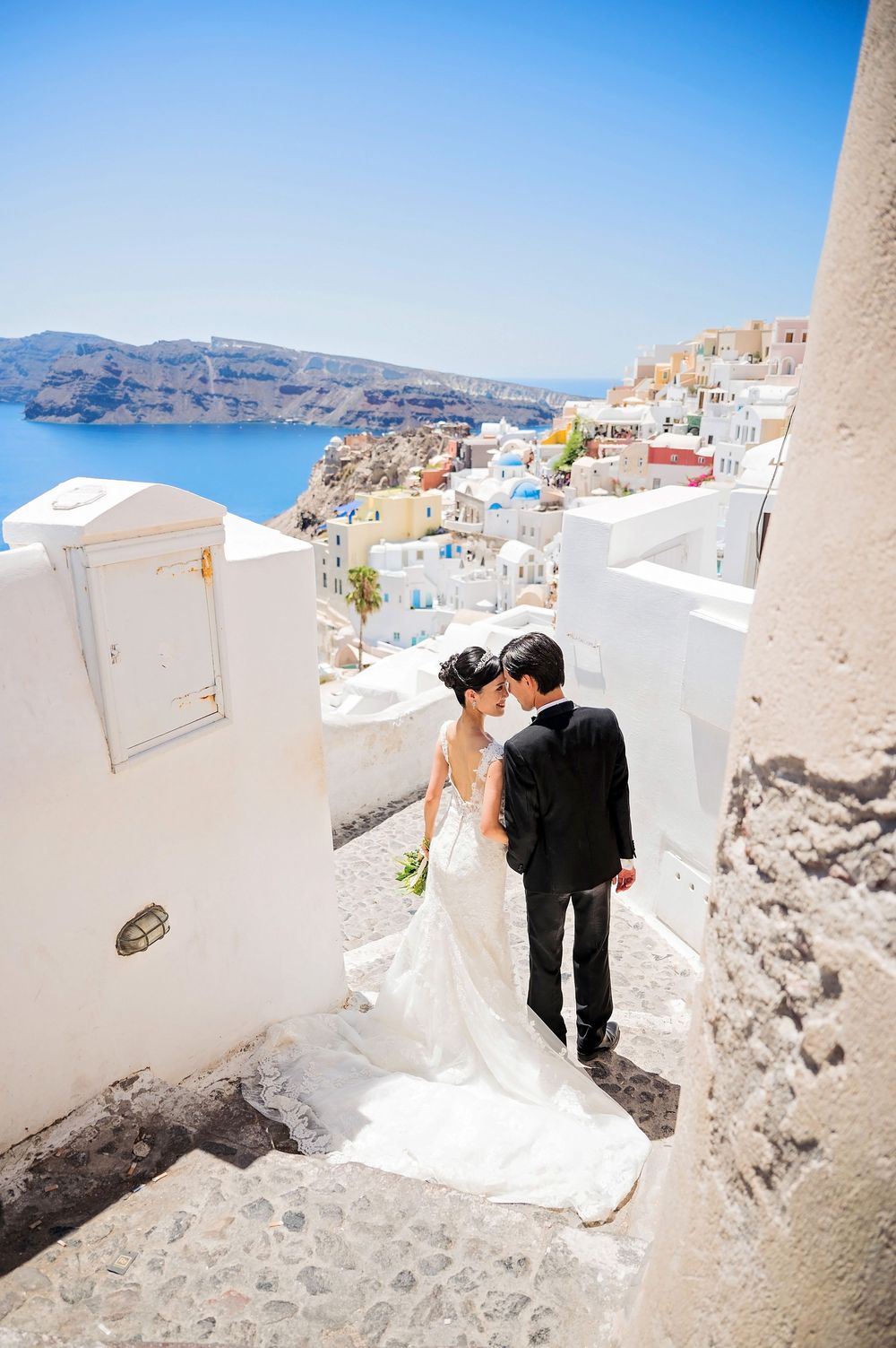 Wedding portrait on white steps of Santorini with classic Mediterranean architecture and sea views.