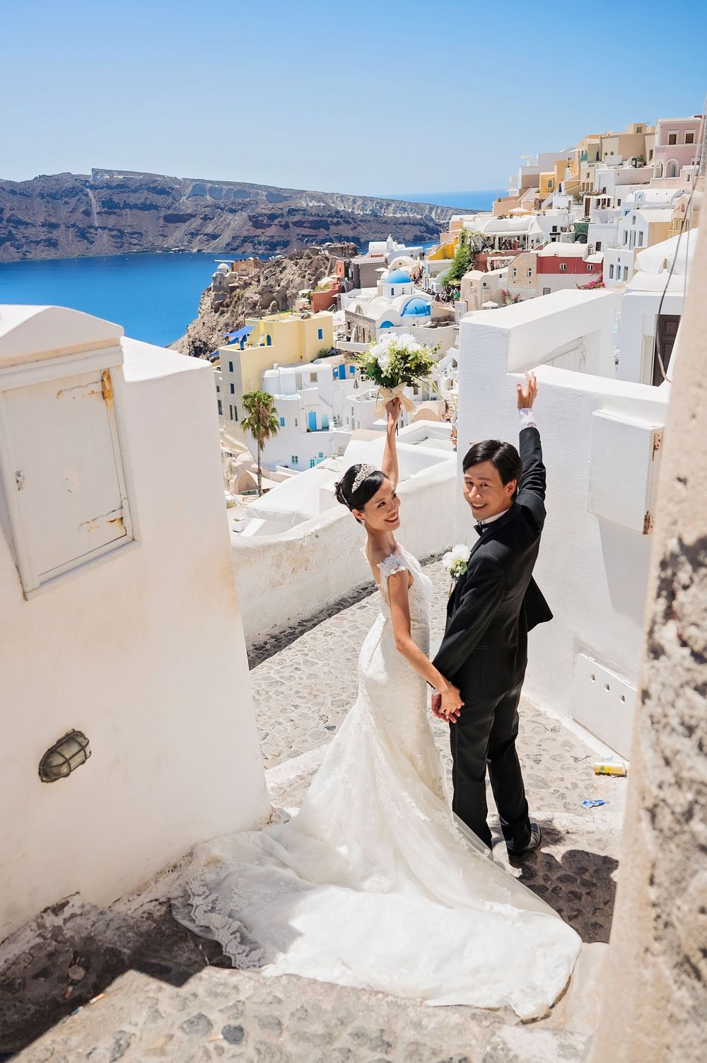 A wedding photo taken on the white-washed steps of Santorini with the blue Aegean Sea and cliffs in the background.