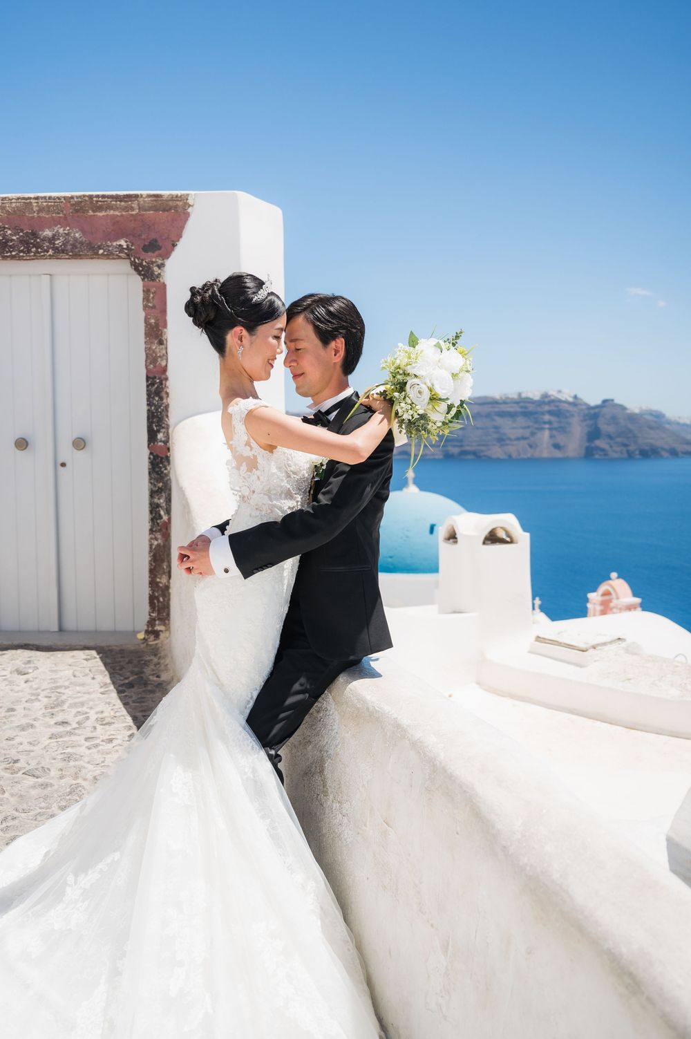 A romantic wedding portrait captured against Santorini's iconic white architecture and blue Mediterranean waters.