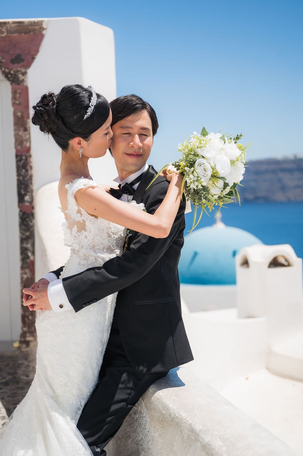 An intimate wedding moment photographed on a white terrace overlooking the Santorini caldera.