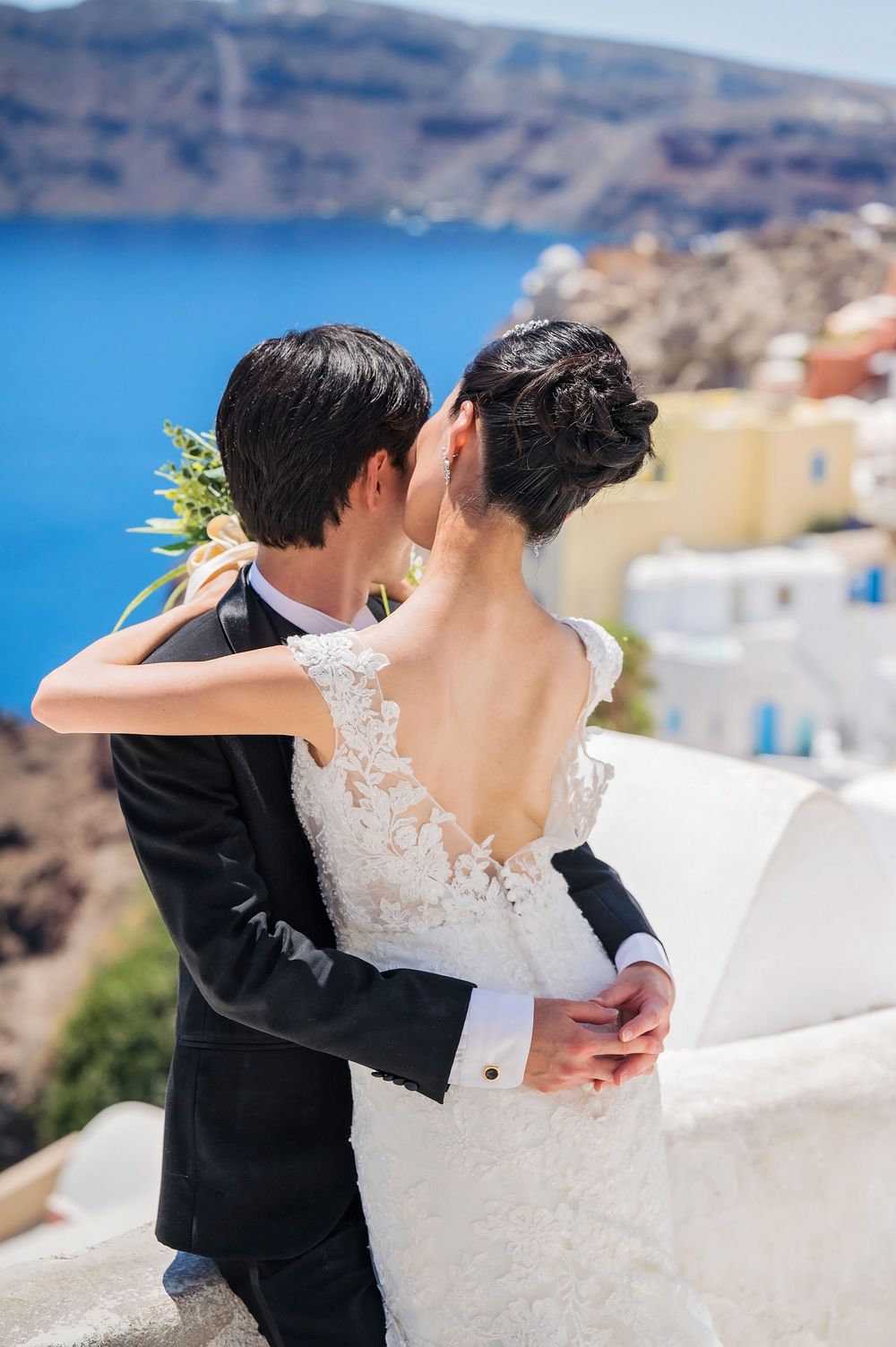 A tender embrace captured on a white terrace with Santorini's blue waters and volcanic cliffs in the background.