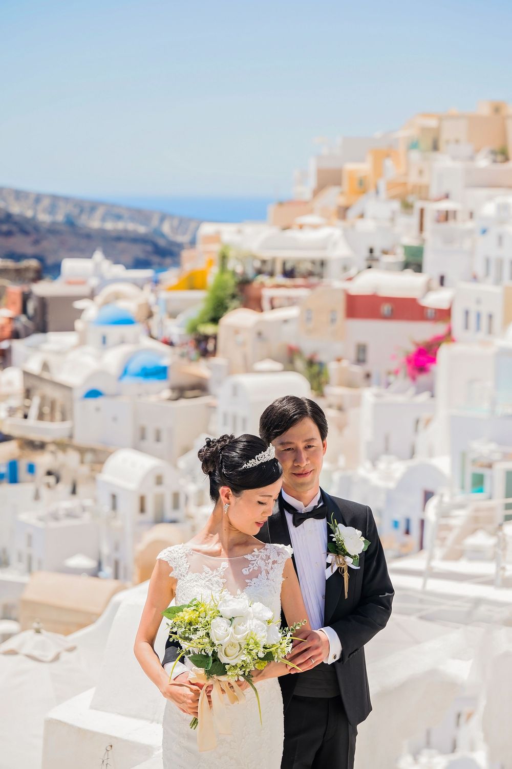 A wedding portrait set against the cascading white buildings and blue domes of Santorini.