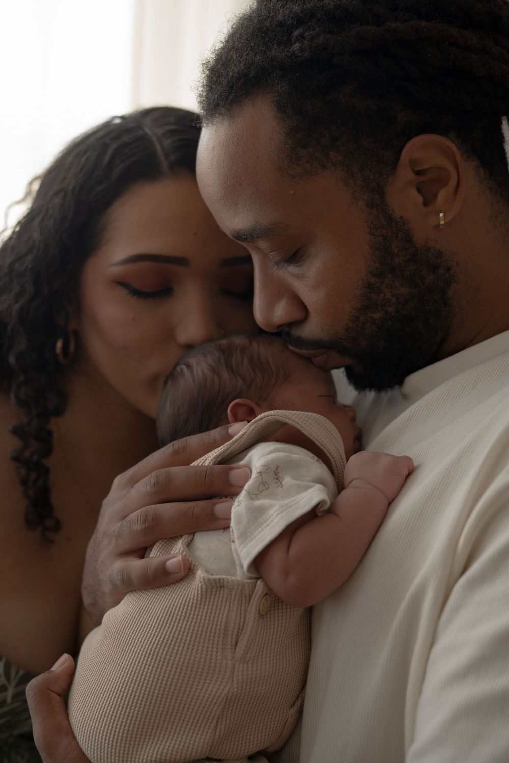 Intimate family moment with sleeping newborn in soft indoor lighting.